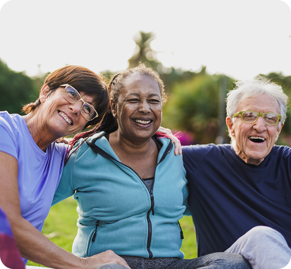 Three diverse senior friends smiling and embracing happily outdoors.