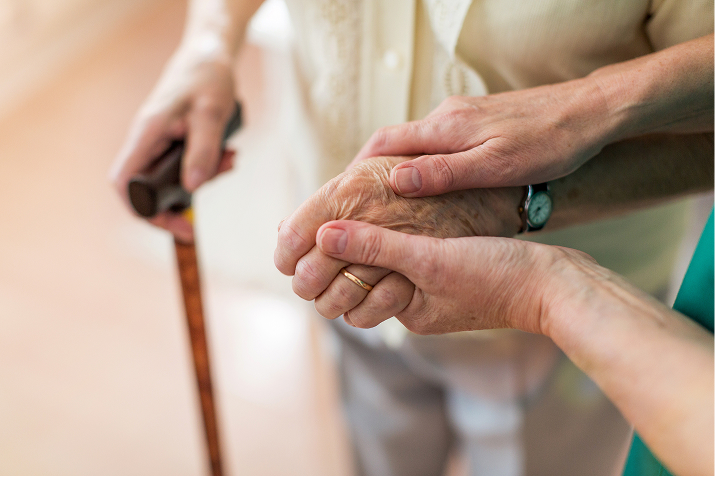 Close-up of a caregiver's hand gently supporting an elderly person's hand holding