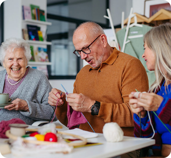 Three cheerful seniors knit and craft together at a table, enjoying their hobby. TITLE