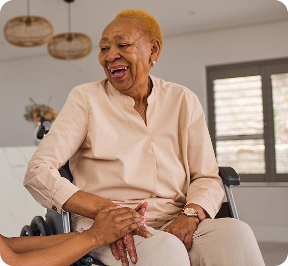 A joyful senior Black woman in a wheelchair laughs while holding hands with a caregiver. TITLE: