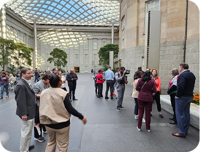 People gather in a spacious, modern indoor atrium featuring a distinctive glass-paneled roof