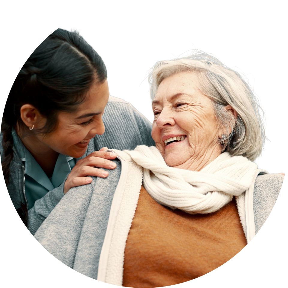 A younger woman gently touches an older woman's shoulder as they both smile happily. TITLE