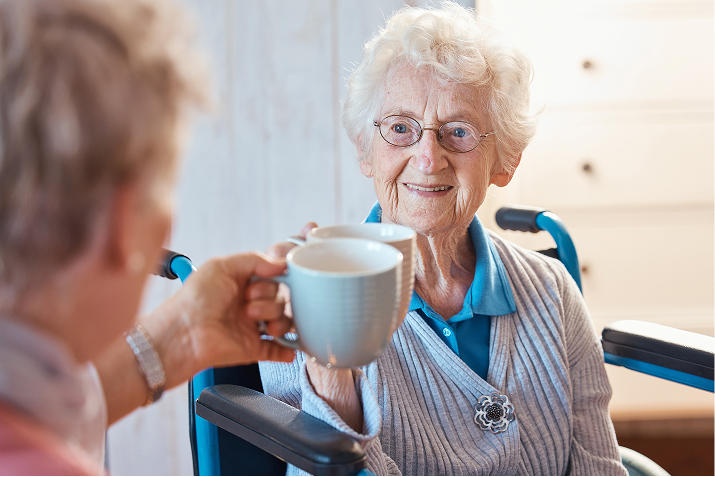 A happy senior woman in a wheelchair toasts mugs with a companion.