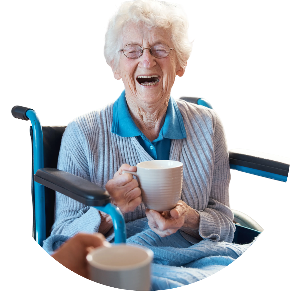 Joyful senior woman in a wheelchair laughs heartily, holding a mug while another is offered.