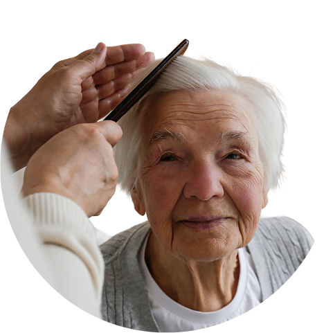 A smiling elderly woman with white hair has her hair gently combed by another person.