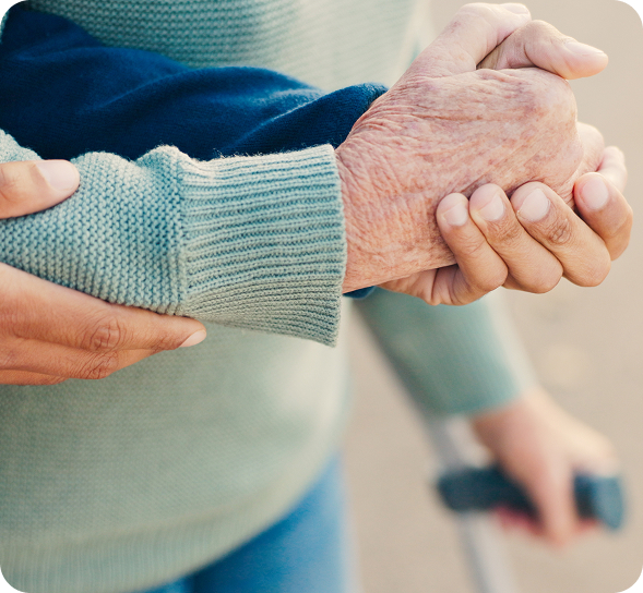 A younger hand gently supports an elder's wrinkled hand, with a walking cane