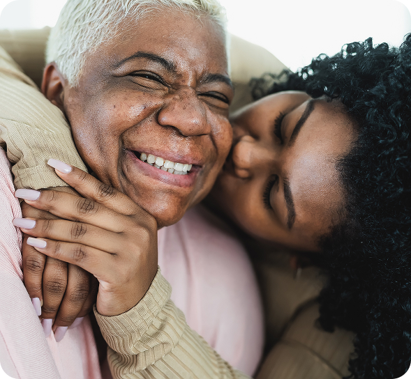 A smiling older Black woman embraces a younger woman who is affectionately kissing her cheek. TITLE