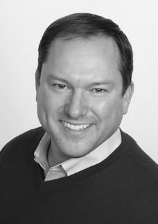 A black and white photo of a man smiling.