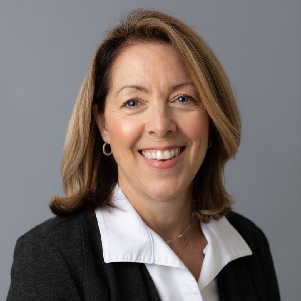 A woman in black jacket and white shirt smiling.